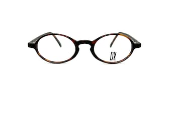 Könnte beinhalten: Oval geformte Brille mit Schildpattmuster auf dem Rahmen. Die Gläser sind klar, und die Bügel sind dunkelbraun. Das Markenlogo "DV" ist auf dem rechten Glas aufgedruckt. Auf weißem Hintergrund.
