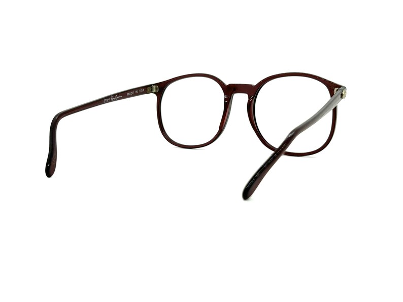 May include: A pair of brown, round spectacles with clear lenses. The glasses have a thin, metal frame and are made in the USA.