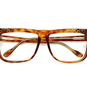 May include: Tortoise shell eyeglasses with gold accents and a leopard print design on the temples. The glasses have a square shape and clear lenses.