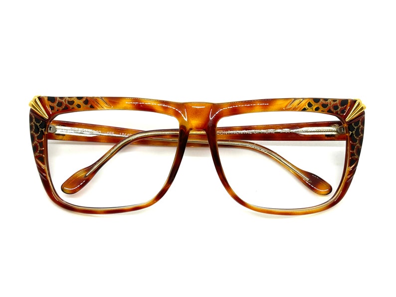 May include: Tortoise shell eyeglasses with gold accents and a leopard print design on the temples. The glasses have a square shape and clear lenses.
