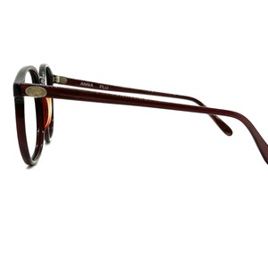 May include: A pair of brown and black round eyeglasses with a silver accent on the side. The glasses have the text "ANNA PLU" printed on the side.