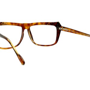 May include: Brown tortoise shell eyeglasses with a gold accent on the bridge. The glasses have a rectangular frame and are shown from the side.