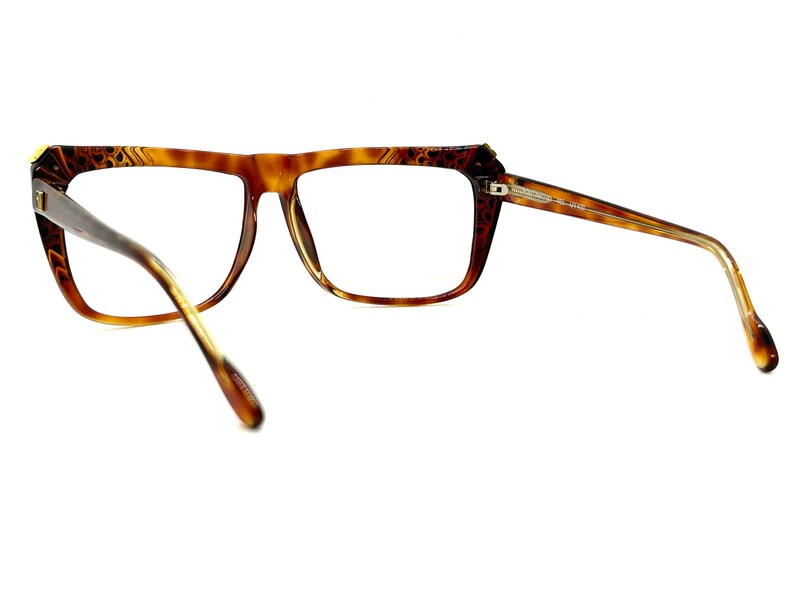 May include: Brown tortoise shell eyeglasses with a gold accent on the bridge. The glasses have a rectangular frame and are shown from the side.