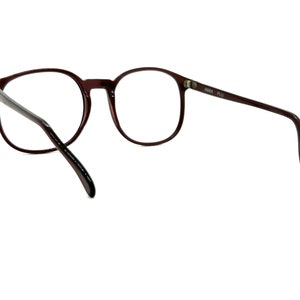 May include: A pair of brown round spectacles with a clear lens. The glasses have a thin metal frame and are made of plastic.