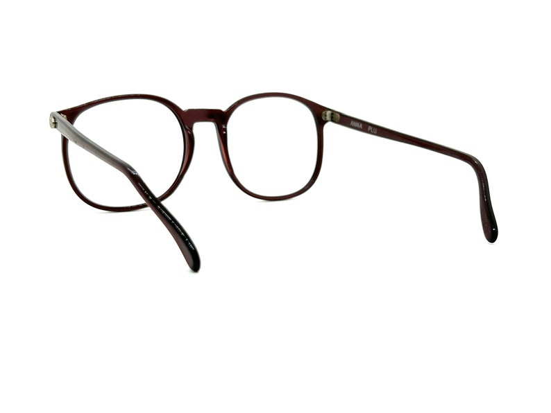 May include: A pair of brown round spectacles with a clear lens. The glasses have a thin metal frame and are made of plastic.