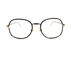May include: Round eyeglasses with a tortoiseshell pattern on the rims and a gold-colored bridge and temples. The lenses are clear, and the overall design is vintage-inspired.