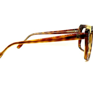 May include: A pair of tortoiseshell eyeglasses with gold accents. The glasses have a rectangular frame and are in a side view.