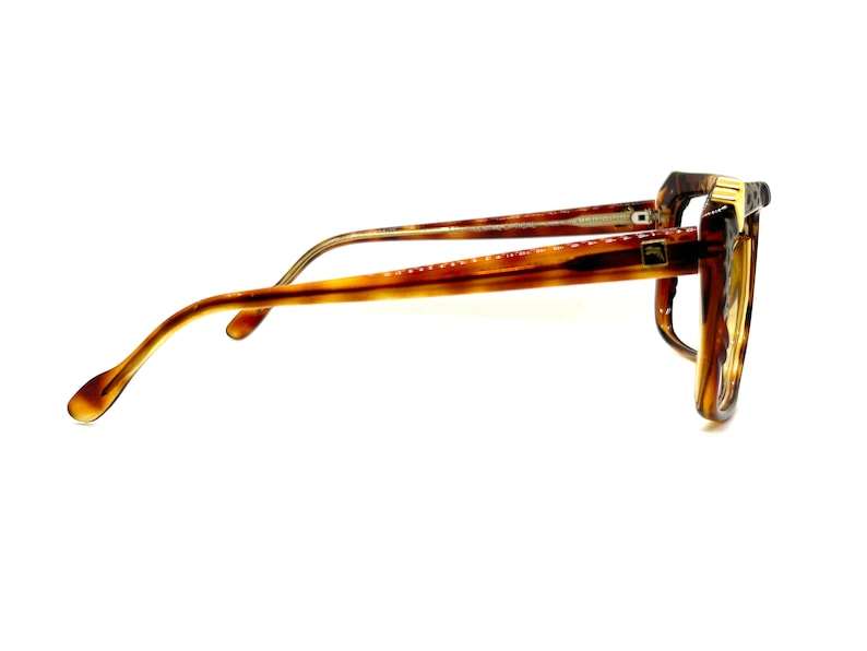 May include: A pair of tortoiseshell eyeglasses with gold accents. The glasses have a rectangular frame and are in a side view.