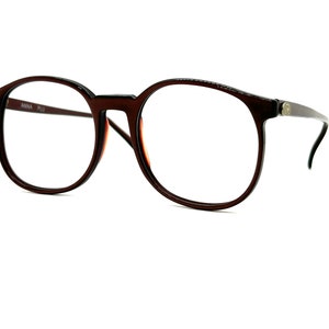 May include: Brown plastic framed spectacles with round lenses. The frames have a subtle tortoiseshell pattern.