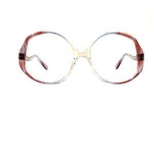 May include: Large, retro-style eyeglasses. The frames have a colour gradient, shifting from reddish-brown to light blue. The lenses are clear, and the arms are slender. A vintage accessory, perfect for a statement look.