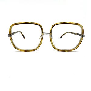 May include: Oversized square eyeglasses featuring a translucent brown and yellow tortoiseshell pattern frame. The glasses have a thin metal bridge and matching tortoiseshell temples with visible metal hinges, providing a classic look with clear lenses.