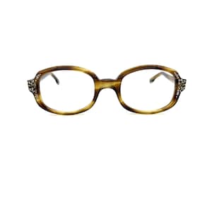 May include: Oval-shaped eyeglasses with a tortoiseshell pattern. The frames have a decorative embellishment of small, sparkling stones on each side. The lenses are clear, and the overall design is vintage-inspired.