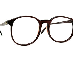 May include: Brown round eyeglasses with a dark brown frame and clear lenses. The glasses have a small gold logo on the left temple and the text "Vogue Eye Wear MADE IN USA" on the right temple.