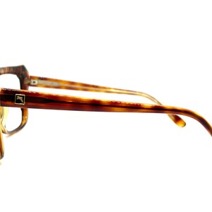 May include: Tortoise shell eyeglasses with gold accents. The glasses have a square frame and are shown from the side.