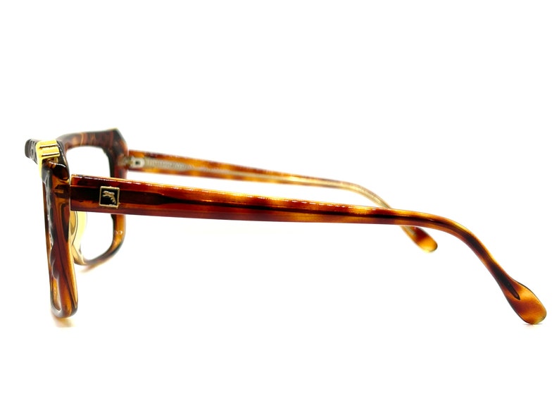 May include: Tortoise shell eyeglasses with gold accents. The glasses have a square frame and are shown from the side.