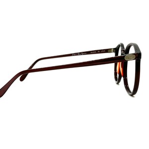 May include: A pair of brown and black round eyeglasses with a silver logo on the side. The glasses are made in the USA.