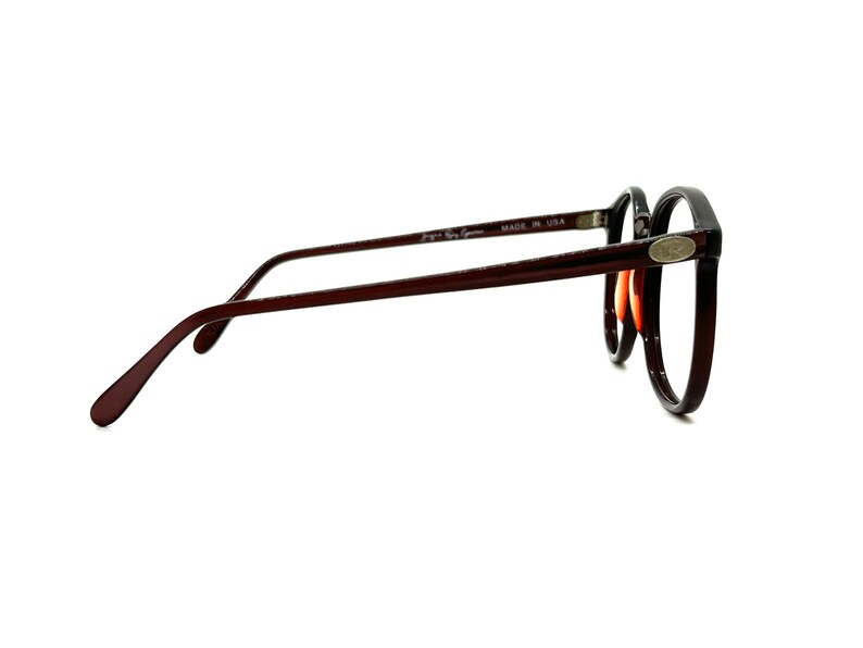 May include: A pair of brown and black round eyeglasses with a silver logo on the side. The glasses are made in the USA.