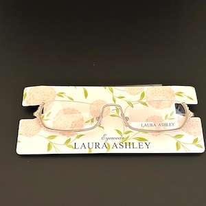 May include: A pair of gold-toned reading glasses with a floral design on the packaging. The packaging says "Laura Ashley Eyewear".