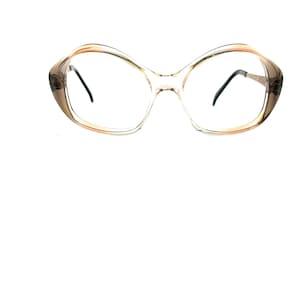 May include: Clear-framed eyeglasses with a butterfly-shaped design. The frames have a gradient color, transitioning from a light brown to a clear hue. The lenses are clear, and the arms are a dark color.