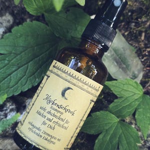 Könnte beinhalten: Eine braune Glassprühflasche mit schwarzem Sprühkopf und einem beigen Etikett, das eine Mondsichel zeigt. Der Text auf dem Etikett lautet Mückenschreck Raumspray, wirkt abschreckend für Mücken und erfrischend für Dich, wirkungsvolles Zitronengras mit erfrischendem Eukalyptus.