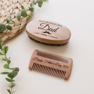 May include: A wooden beard brush and comb set. The oval brush is engraved with "You're The World's Best Dad" and a mustache graphic. The comb is engraved with "Happy Father's Day 2024". The set is made of light brown wood.