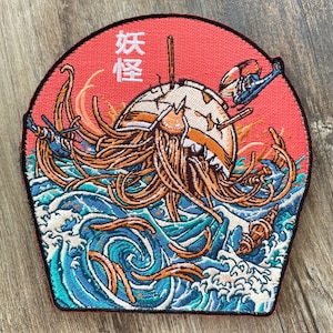 Peut inclure: Un patch brodé rouge, blanc et bleu avec un motif de vague de style japonais et une créature avec des tentacules. Le texte "妖怪" est brodé en blanc sur le patch.