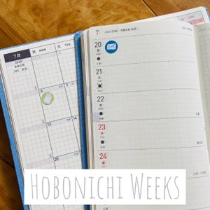 May include: A close-up of a Hobonichi Weeks planner open to July 2020. The planner has a blue cover and a white interior with a grid pattern. The date is written in Japanese and English. The planner has a small envelope icon on the 20th.
