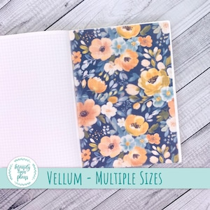 May include: Open notebook with a vellum overlay featuring a floral design. The vellum has a navy blue background with orange, yellow, and blue flowers. The notebook's left page is blank with a grid pattern. Text on the image reads "Vellum - Multiple Sizes."