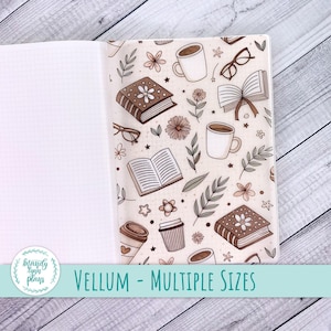 Puede incluir: Cuaderno abierto con una cubierta de vitela con un patrón repetido de libros, tazas de café, gafas y flores en tonos marrones y beige. El texto "VELLUM - MULTIPLE SIZES" se muestra en la parte inferior de la imagen.