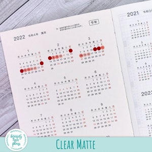 May include: A close-up of a clear matte calendar planner with red circles highlighting the dates. The calendar is for the years 2021 and 2022. The months are labeled in Japanese.