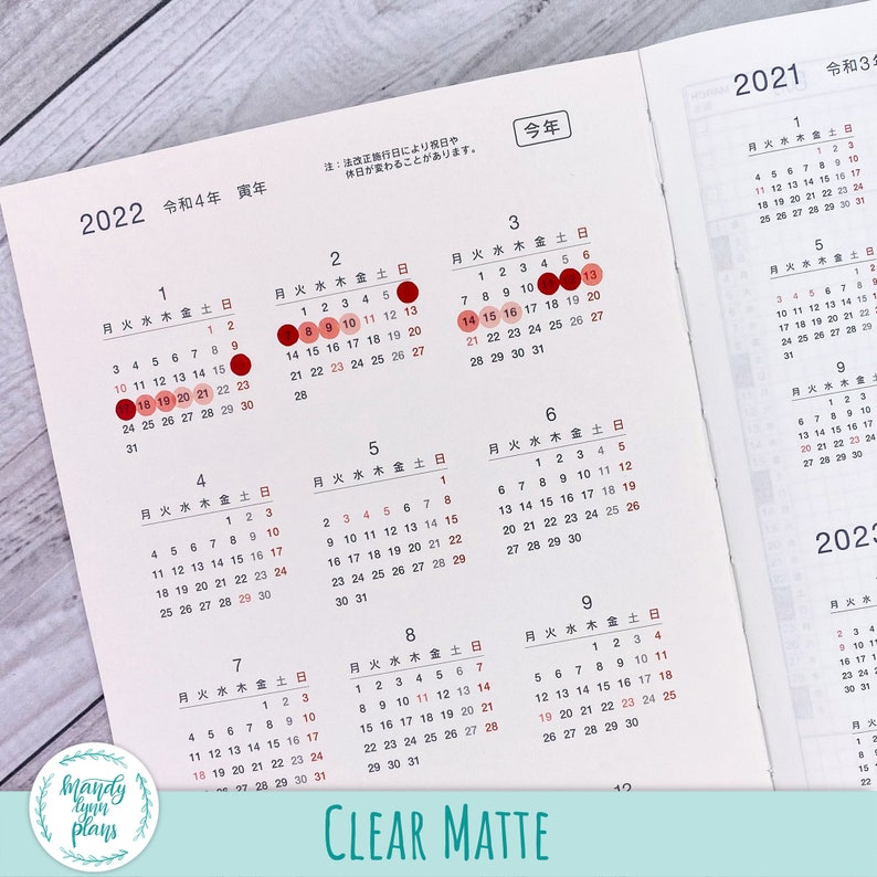 May include: A close-up of a clear matte calendar planner with red circles highlighting the dates. The calendar is for the years 2021 and 2022. The months are labeled in Japanese.