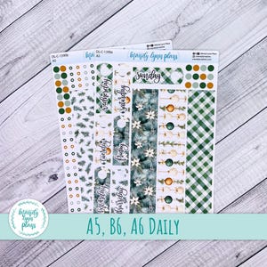 May include: Two A5 sticker sheets labeled DL-C-1390a and DL-C-1390b by mandy lynn plans. The sheets feature holiday-themed designs including green plaid patterns, pine branches, poinsettias, and Christmas ornaments, with text for days of the week.