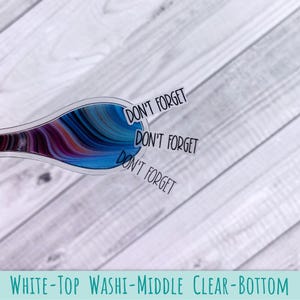 May include: A clear sticker featuring a swirling abstract pattern of blue, purple, and black colors. The sticker has a rounded shape and includes the text DON'T FORGET printed three times in a black sans-serif font extending from the right side.