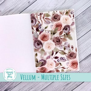 Puede incluir: Cuaderno abierto con una cubierta floral de vitela. La cubierta presenta rosas de acuarela en tonos malva, melocotón y crema, con hojas verdes y bayas moradas. El texto "VELLUM - MULTIPLE SIZES" se muestra en la parte inferior.