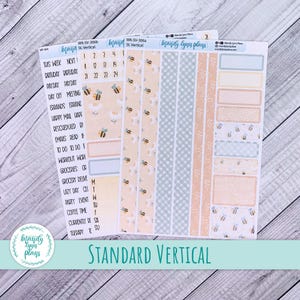 Puede incluir: Un conjunto de pegatinas para planificador con temática de abejas. Las pegatinas presentan varios diseños, incluyendo tiras estampadas, cajas y etiquetas. La paleta de colores incluye tonos pastel de melocotón, azul y amarillo. El texto "Standard Vertical" está en la parte inferior.