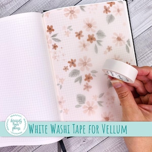 May include: A roll of white washi tape held over an open notebook with grid paper and a translucent vellum sheet featuring a repeating pattern of small, soft-toned orange flowers and muted green leaves. The text reads Mandy Lynn Plans.
