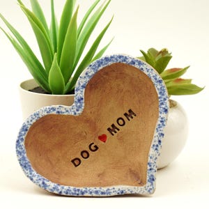 May include: A heart-shaped ceramic dish with a blue and white speckled glaze. The dish has the words "DOG MOM" inscribed on it with a red heart between the words.