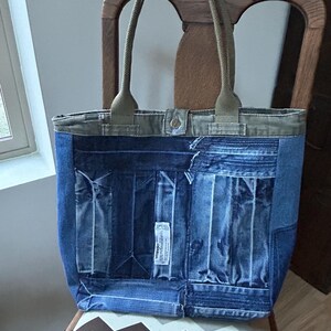Puede incluir: Un bolso tote de mezclilla con detalles y asas de color verde oliva. El bolso est&aacute; hecho de mezclilla reciclada, con bolsillos y una etiqueta Wrangler. El bolso est&aacute; sobre una silla estampada.