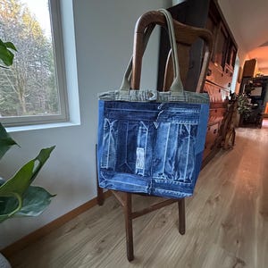Puede incluir: Un bolso tote de mezclilla con un dise&ntilde;o de patchwork, con un cuerpo de mezclilla azul claro y una parte superior de mezclilla m&aacute;s clara con asas beige. La bolsa est&aacute; sobre una silla de madera en una habitaci&oacute;n bien iluminada.