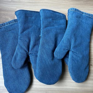 May include: Three oven mitts crafted from blue denim fabric. Each mitt features a standard thumb-separated design with a stitched hem at the opening. The denim material displays a consistent medium-blue wash with visible diagonal twill texture.