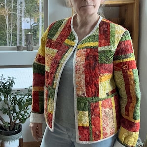 May include: A quilted jacket with a patchwork design in shades of red, green, yellow, and white. The jacket has a white collar and a button closure.