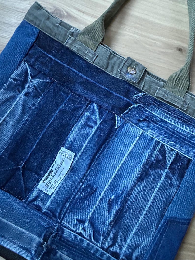 Puede incluir: Bolso tote de mezclilla con dise&ntilde;o de patchwork. El bolso presenta una variedad de lavados de mezclilla azul, con una parte superior y correas de lona verde. Una peque&ntilde;a etiqueta blanca con texto negro es visible en la parte delantera.