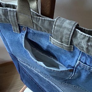 Puede incluir: Un bolso tote de mezclilla en azul claro con un bolsillo azul m&aacute;s oscuro. Tiene asas y ribetes de lona verde oliva. El bolsillo interior es visible y la bolsa parece estar hecha de mezclilla reciclada.