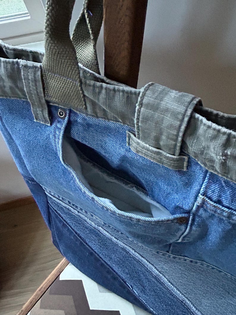 Puede incluir: Un bolso tote de mezclilla en azul claro con un bolsillo azul m&aacute;s oscuro. Tiene asas y ribetes de lona verde oliva. El bolsillo interior es visible y la bolsa parece estar hecha de mezclilla reciclada.