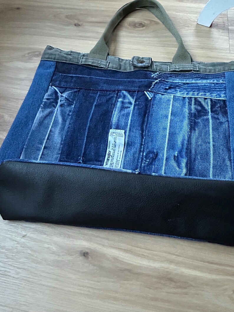 Puede incluir: Bolso tote de mezclilla con dise&ntilde;o patchwork. El bolso presenta una variedad de lavados de mezclilla azul, una base negra y asas verde oliva. Una peque&ntilde;a etiqueta blanca es visible en la parte delantera.