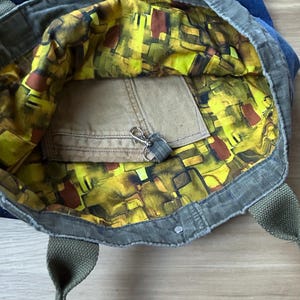 Puede incluir: Bolso tote abierto con exterior verde e interior estampado en amarillo, marr&oacute;n y verde vibrantes. El bolso tiene un peque&ntilde;o bolsillo y un llavero. Las asas son verdes.