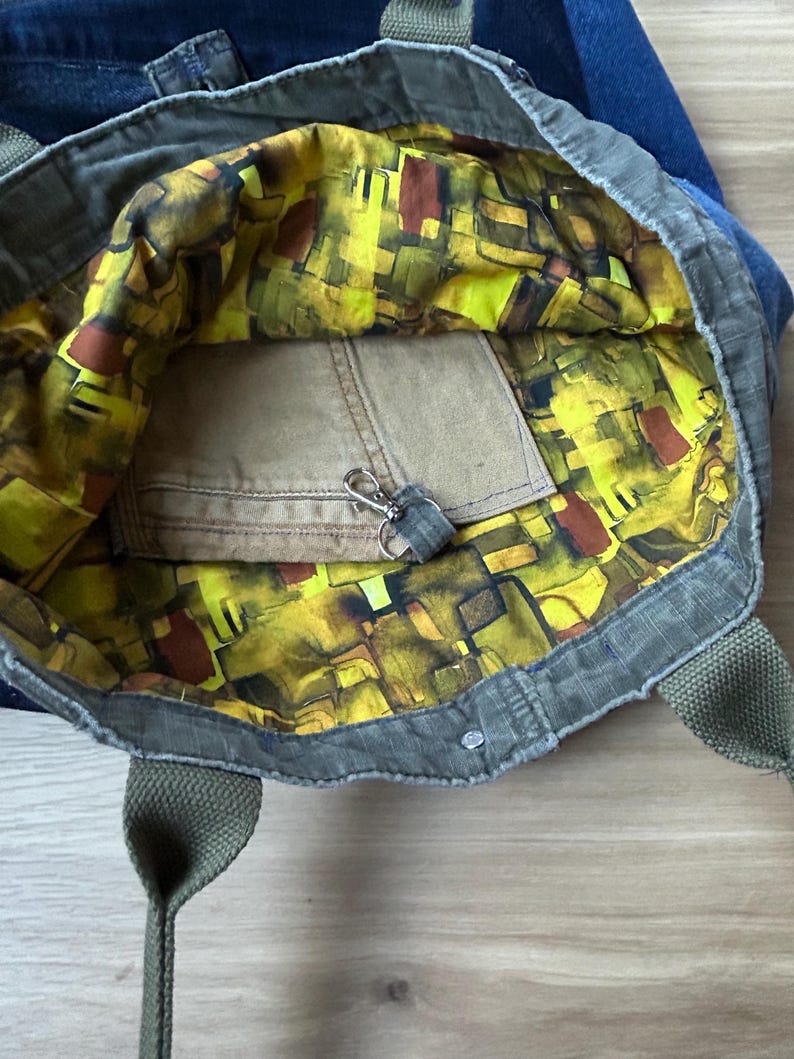 Puede incluir: Bolso tote abierto con exterior verde e interior estampado en amarillo, marr&oacute;n y verde vibrantes. El bolso tiene un peque&ntilde;o bolsillo y un llavero. Las asas son verdes.