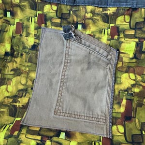 Puede incluir: Bolso tote hecho a mano con un dise&ntilde;o &uacute;nico. El bolso presenta un colorido patr&oacute;n abstracto en tonos amarillos, verdes y marrones. Tiene un bolsillo beige y correas verde oliva. Un llavero plateado est&aacute; sujeto al bolsillo.
