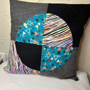 May include: A square pillow with a black, gray, and white geometric pattern. The pillow is made of different fabrics and has a zipper closure.