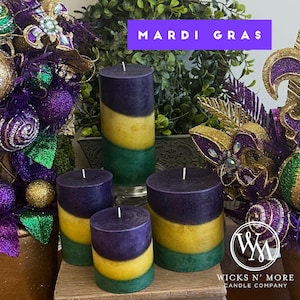 May include: Four Mardi Gras themed candles with purple, gold, and green stripes. The candles are arranged on a wooden surface with Mardi Gras decorations in the background. The text "Mardi Gras" is visible in the image.